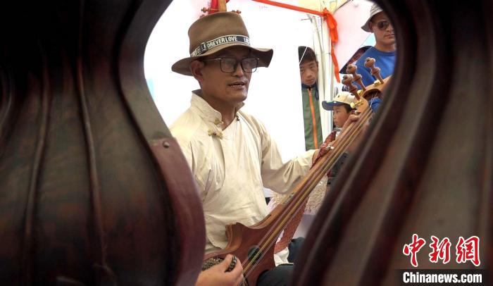 图为商贩边卖民族乐器，边弹唱当地经典民歌。　贡桑拉姆 摄